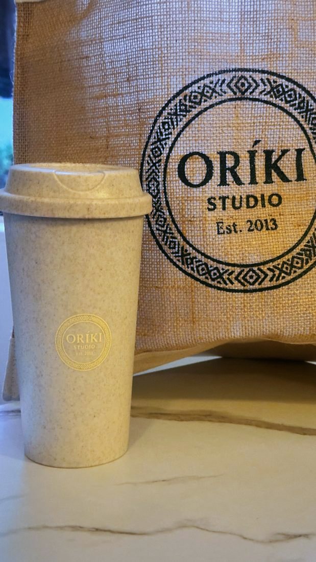 Oríki Studio reusable cup, gold-printed, with jute tote behind
